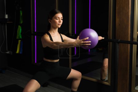 Photo for Attractive caucasian sporty woman taking a barre class exercising with a fitness ball at fitness center with led lighting - Royalty Free Image
