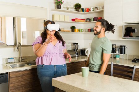 Foto de Hermosa mujer usando gafas de realidad virtual y riendo con su novio mientras se divierten juntos en la cocina - Imagen libre de derechos