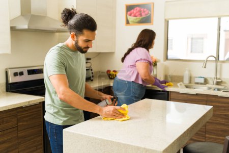 Téléchargez les photos : Beau latin homme nettoyer la cuisine avec sa petite amie tout en appréciant faire le travail à la maison et les corvées ensemble - en image libre de droit