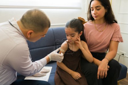 Photo for Mother at home looking at the pediatrician putting a vaccine or medicine injection to her sick little kid during a doctor's visit - Royalty Free Image