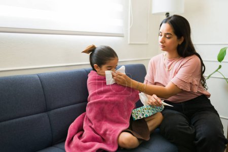 Téléchargez les photos : Belle mère qui mouche son enfant malade de six ans avec une fièvre qui souffre d'un rhume ou d'une grippe enveloppée dans une couverture - en image libre de droit