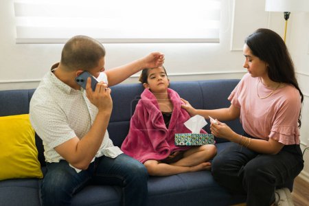 Foto de Familia en casa sintiéndose preocupada por su hijo enfermo de 6 años con fiebre llamando por teléfono para una visita al médico - Imagen libre de derechos