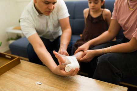 Téléchargez les photos : Gros plan d'une famille dans le salon mettant un bandage sur le pied de leur petit enfant blessé dans la douleur après un accident - en image libre de droit