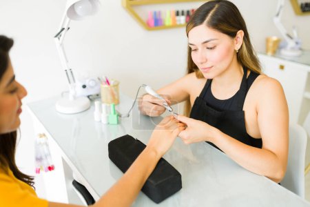 Photo for Happy latin woman doing a manicure using an electric nail polisher before painting the nails using uv lighting - Royalty Free Image