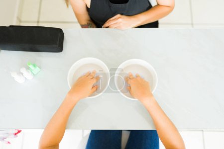 Photo for Top view of a woman client soaking her hands in salt water during a relaxing manicure spa service at the nail salon - Royalty Free Image