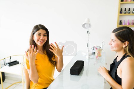 Foto de Mujer joven emocionada sonriendo mostrando sus hermosas uñas después de una manicura profesional en el salón de manicura - Imagen libre de derechos
