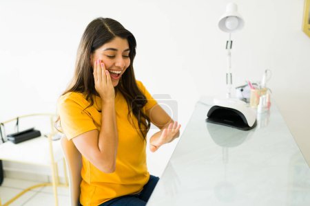 Téléchargez les photos : Joyeux jeune femme regardant excité dans le salon des ongles en raison de sa belle couleur de gel uv et service de manucure - en image libre de droit