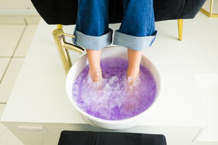 Foto de Primer plano de una joven latina empapándose los pies en sales de gel para exfoliarse los pies durante un relajante servicio de pedicura - Imagen libre de derechos