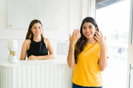 Téléchargez les photos : Attrayant jeune femme souriant regardant heureux et satisfait de son service d'ongles et de manucure avec la couleur de gel dans le salon de beauté - en image libre de droit