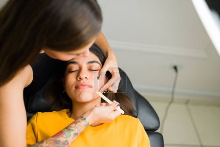Téléchargez les photos : Cosmetologue utilisant de la cire pour l'épilation sur la lèvre supérieure d'un client détendu dans le salon de beauté - en image libre de droit