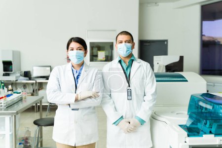 Foto de Equipo de químicos profesionales con batas de laboratorio, mascarillas y guantes mirando a la cámara que trabaja en un laboratorio médico - Imagen libre de derechos
