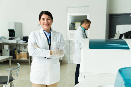 Foto de Atractiva mujer caucásica luciendo feliz trabajando como química en el laboratorio médico usando una bata de laboratorio haciendo análisis de sangre - Imagen libre de derechos