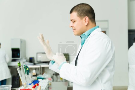 Téléchargez les photos : Chimiste professionnel hispanique avec une blouse blanche portant des gants travaillant dans un laboratoire médical faisant des tests médicaux sanguins - en image libre de droit