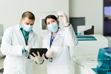Téléchargez les photos : Femme chimiste tenant un échantillon de sang dans une éprouvette tout en vérifiant les résultats médicaux avec un technicien dans le laboratoire médical - en image libre de droit