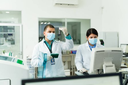Foto de Equipo de químicos o técnicos de laboratorio que usan el equipo mientras usan muestras de sangre en tubos de ensayo para hacer pruebas médicas - Imagen libre de derechos