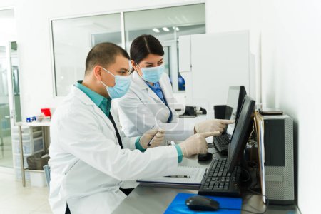 Foto de Mujer caucásica y hombre latino trabajando juntos como químicos usando muestras de sangre en tubos de ensayo en el laboratorio médico - Imagen libre de derechos