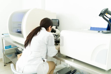 Foto de Vista trasera de una mujer y un químico profesional mirando una muestra médica en el microscopio y el equipo de laboratorio - Imagen libre de derechos