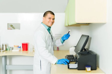 Téléchargez les photos : Joyeux homme heureux souriant travaillant comme chimiste dans le laboratoire médical et tenant un échantillon de sang dans le tube à essai regardant joyeux - en image libre de droit
