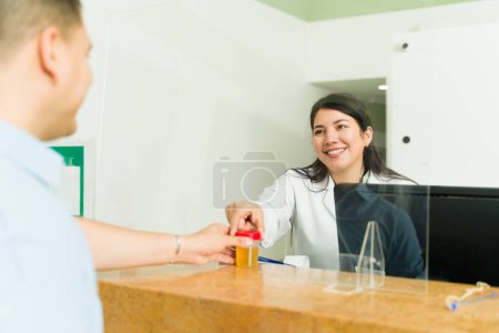Foto de Mujer joven emocionada trabajando en el escritorio del laboratorio médico que recibe una prueba de orina de una paciente y sonriendo - Imagen libre de derechos