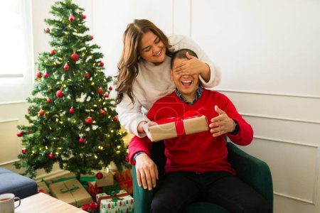 Téléchargez les photos : Femme excitée plus la taille couvrant les yeux de son petit ami et donnant une surprise beau cadeau à son mari pour Noël - en image libre de droit