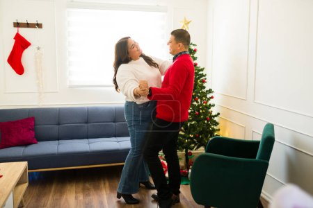Photo for Romantic happy couple dancing in the living room and smiling feeling in love while celebrating the holidays at home - Royalty Free Image