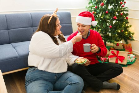 Téléchargez les photos : Grosse femme et homme mexicain mangeant de délicieux biscuits de vacances et buvant du chocolat chaud ensemble tout en se relaxant pendant Noël - en image libre de droit