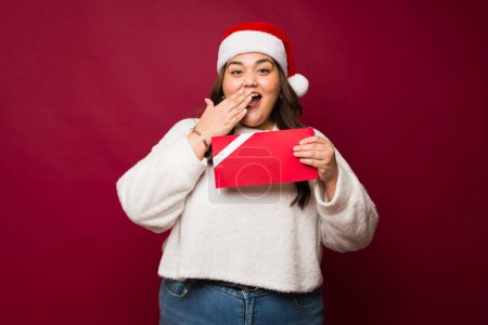 Foto de Sorprendido más tamaño mujer cubriendo su boca excitado durante la Navidad acerca de recibir un certificado de regalo de maqueta como un regalo - Imagen libre de derechos