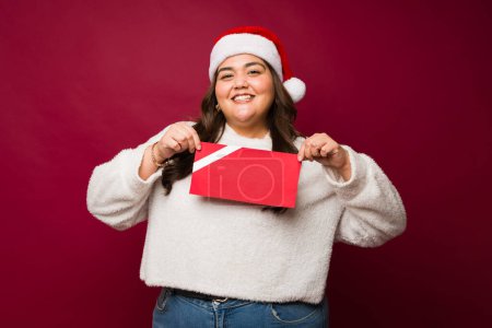 Téléchargez les photos : Fat excité femme mexicaine heureux de recevoir une carte cadeau rouge maquette pendant les vacances de Noël - en image libre de droit
