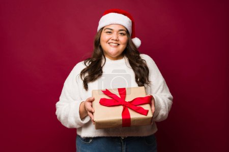 Photo for Beautiful fat latin woman smiling making eye contact and giving a beautiful christmas present while celebrating the holidays - Royalty Free Image
