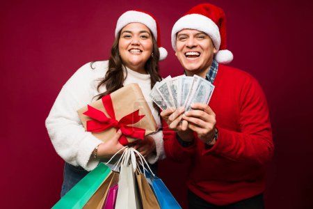 Foto de Emocionada hermosa pareja celebrando las fiestas de Navidad llevando regalos y bolsas de compras con mucho dinero - Imagen libre de derechos