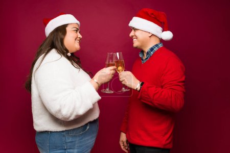 Téléchargez les photos : Gros hispanique femme et heureux homme griller boire du champagne tout en disant acclamations souriant pendant les vacances de Noël - en image libre de droit