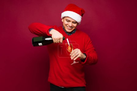 Photo for Attractive man serving a drink in a champagne flute against a red studio background and celebrating christmas during a party - Royalty Free Image