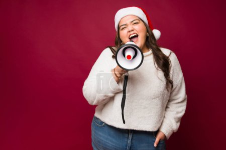 Téléchargez les photos : Mexicain attrayant grosse femme hurlant donnant un message de Noël en utilisant un mégaphone regardant très heureux - en image libre de droit