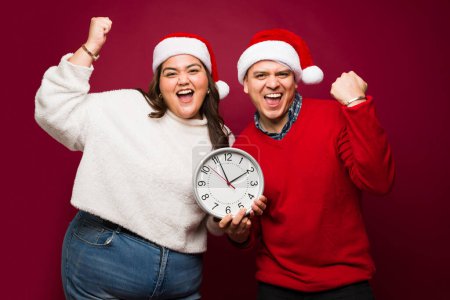 Foto de Feliz feliz pareja latina emocionada celebrando la celebración de un reloj haciendo una cuenta regresiva para las vacaciones de Navidad - Imagen libre de derechos