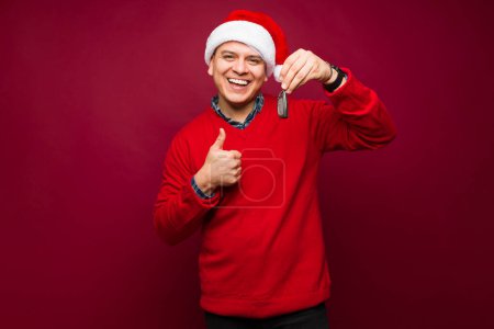 Foto de Guapo emocionado mexicano con un sombrero de santa mostrando las llaves de su coche después de comprar un coche nuevo durante la Navidad - Imagen libre de derechos