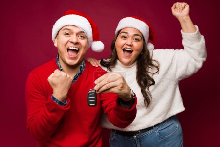 Téléchargez les photos : Heureux couple hispanique regardant excité et célébrer l'achat d'une nouvelle voiture pendant les vacances de Noël - en image libre de droit