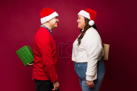 Téléchargez les photos : Vue latérale d'un beau couple heureux se donnant des cadeaux de Noël et souriant heureux pour les vacances - en image libre de droit