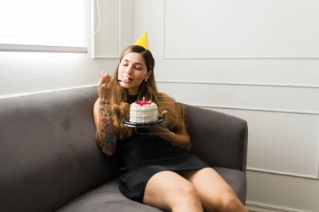 Foto de Relajado hermosa mujer buscando feliz mientras disfruta de comer su pastel de cumpleaños solo y relajarse solo en casa - Imagen libre de derechos