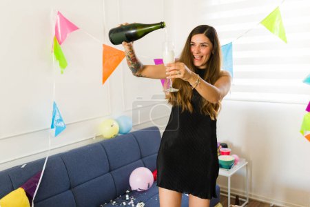 Foto de Feliz mujer latina bebiendo champán y celebrando una fiesta sintiéndose emocionada y borracha por la mañana durante una fiesta de cumpleaños - Imagen libre de derechos