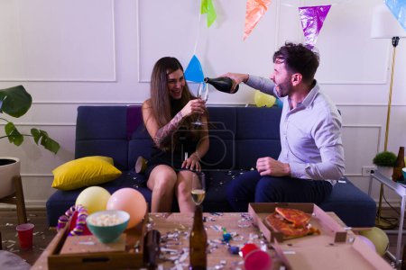 Foto de Atractiva pareja feliz aspecto emocionado mientras dice vítores beber champán juntos por la noche durante una fiesta de cumpleaños en casa celebrando - Imagen libre de derechos