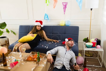 Foto de Pareja dormida con sombreros de santa dormir inconsciente en el sofá después de beber mucho alcohol durante una fiesta de Navidad - Imagen libre de derechos