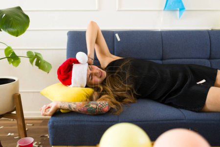 Photo for Sick latin woman waking up with a hangover and headache after drinking a lot of alcohol after celebrating a christmas party - Royalty Free Image