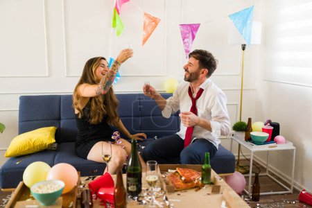 Téléchargez les photos : Couple heureux excité faisant un toast en disant acclamations tout en buvant des coups de tequila célébrant lors d'une fête l'air ivre - en image libre de droit