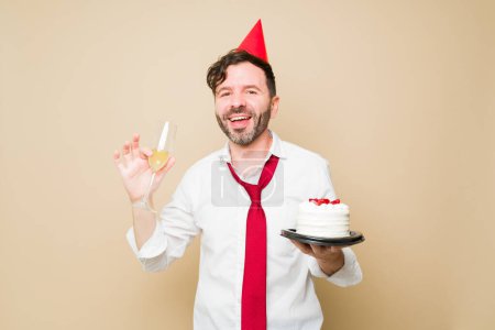 Téléchargez les photos : Souriant homme attrayant regardant heureux célébrer son anniversaire manger du gâteau et boire du vin ou du champagne et s'amuser à une fête - en image libre de droit
