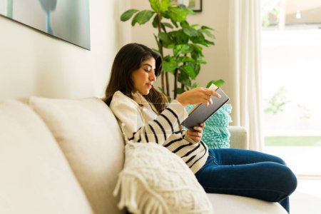 Photo for Smart mexican young woman relaxing on the sofa reading an interesting book about wellness during her leisure time at home - Royalty Free Image