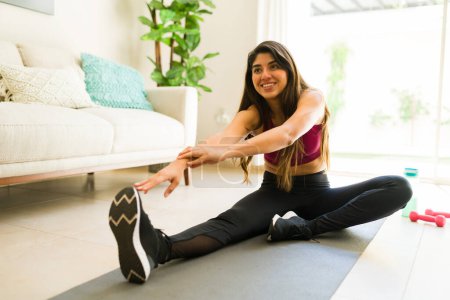 Téléchargez les photos : Joyeux belle jeune femme qui s'étire avant une pratique de yoga à la maison en profitant de son passe-temps de fitness - en image libre de droit