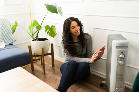 Happy attractive young woman smiling while enjoying the oil radiator and heating at home during the winter weather