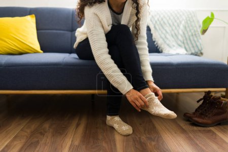 Foto de Primer plano de una mujer joven calentándose durante el clima frío en casa poniéndose calcetines y ropa de invierno mientras está en el sofá de la sala de estar - Imagen libre de derechos