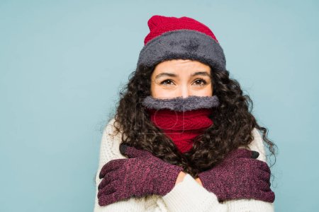 Téléchargez les photos : Femme hispanique très froide avec des cheveux bouclés frissonnant sentir très froid à l'aide d'un chapeau en tricot, écharpe et gants pour le temps d'hiver à côté de copier l'espace publicitaire - en image libre de droit