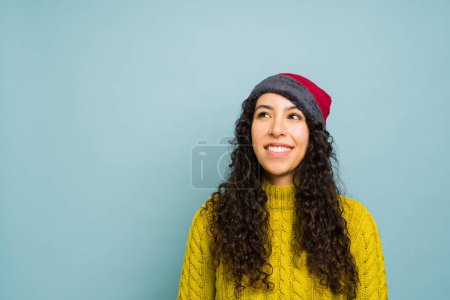 Photo for Attractive latin young woman with a knit hat wearing a yellow sweater and thinking about the cold winter weather with copy space ad - Royalty Free Image